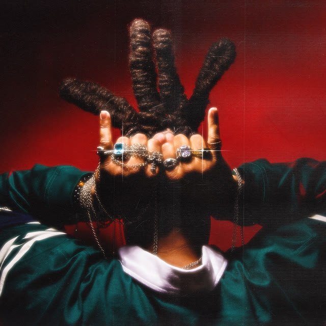 New Devils single cover: a man with locs covering his face with jeweled hands on a red background