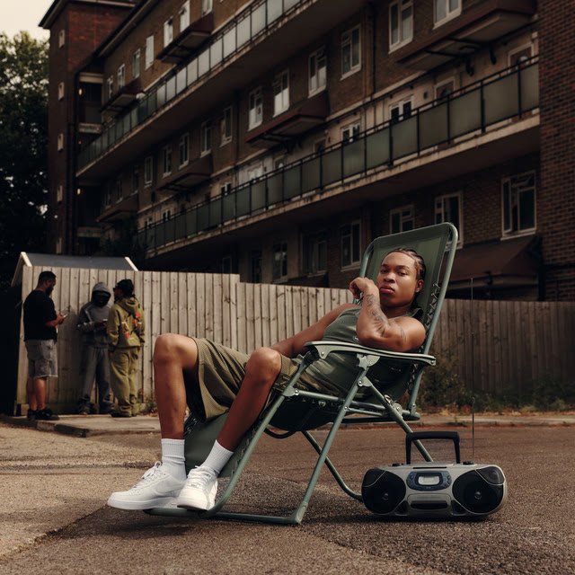 Nippa sitting on a deck chair with a boombox in front of a North London housing estate