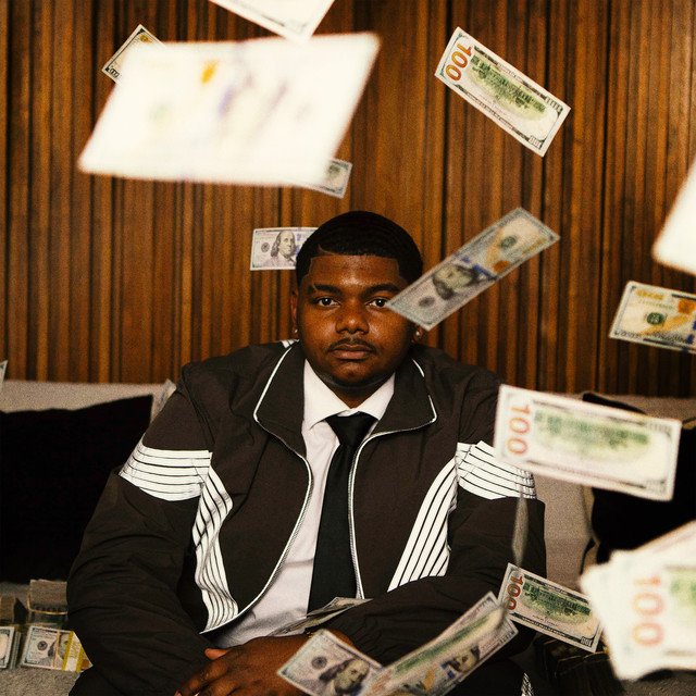 JAZZ MONEY VOL. 2 album cover: Zacchae’us Paul in a striped jacket and tie sitting in a wood-paneled room while hundred-dollar bills fly around him